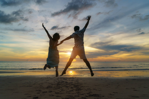 亚洲夫妇跳在海边美丽的日落，夫妇在暑假度假的概念图片下载