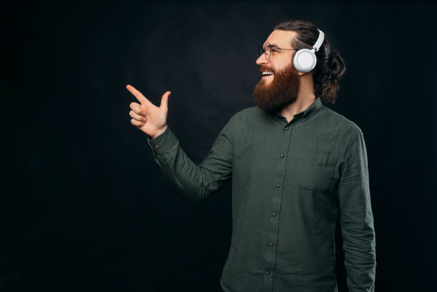 从侧面看，一个戴着眼镜和耳机的大胡子男人正指着一边。图片下载