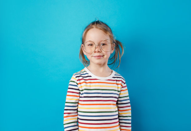 一个戴着大眼镜、穿着条纹t恤的小女孩站在一个孤立的蓝色背景上。图片下载