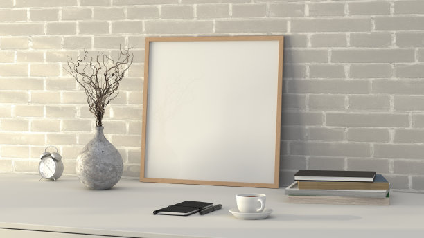 方形木制图片海报框架模型。白色的桌子上有咖啡、书、花瓶和笔记本。白色砖墙背景。图片下载