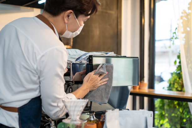 亚洲咖啡馆店主清洁柜台在餐厅咖啡厅重新开业。在新型冠状病毒感染症(covid - 19病毒)封锁结束后，帅气的咖啡师服务员戴上口罩，用消毒剂喷雾对机器进行消毒和擦拭图片下载