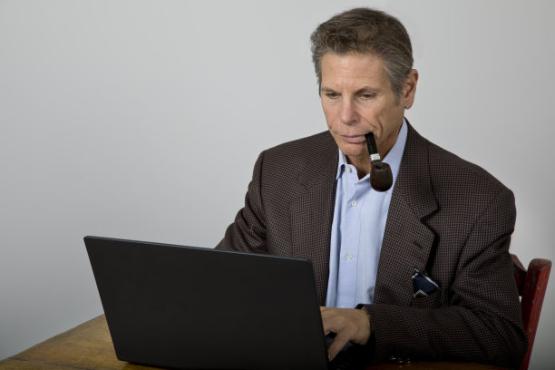 穿着运动夹克的男人抽着烟斗在笔记本电脑前工作图片下载