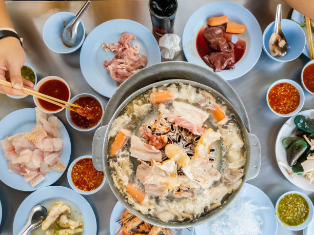 用木筷子夹着烤肉，泰式烤肉在热锅上烧烤，在热炉子上烤猪肉，一个假日家庭在餐馆吃饭。智能手机的照片图片下载