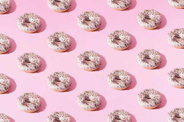 在粉色粉彩的背景上，用白釉和小的彩色碎屑排列环形甜甜圈。最小的概念和设计。模式。图片下载