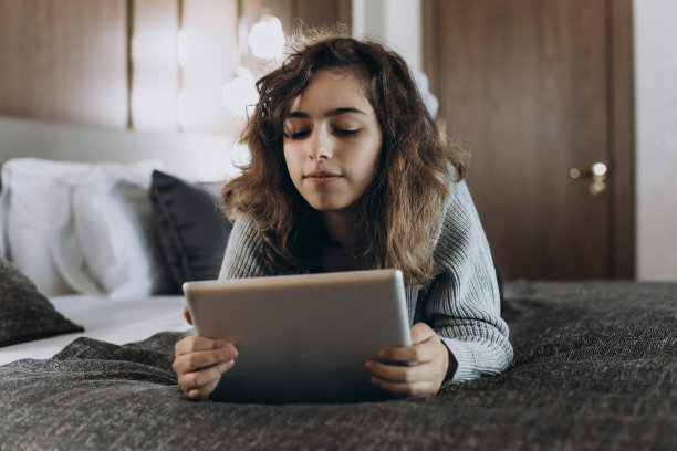 快乐的少女在平板电脑上看视频。与朋友在线聊天。女孩躺在床上图片下载