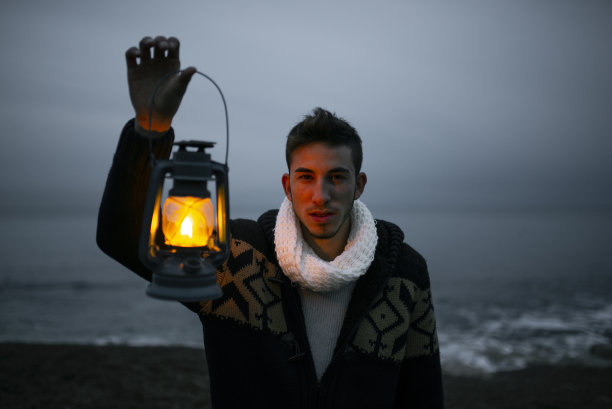 在寒冷的天气里，沙滩上的年轻人举着煤油灯看着相机。图片下载