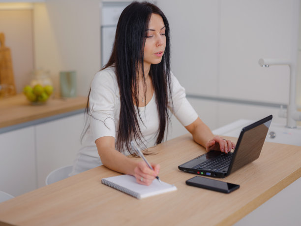 微笑的年轻女子看着厨房的笔记本电脑屏幕图片下载