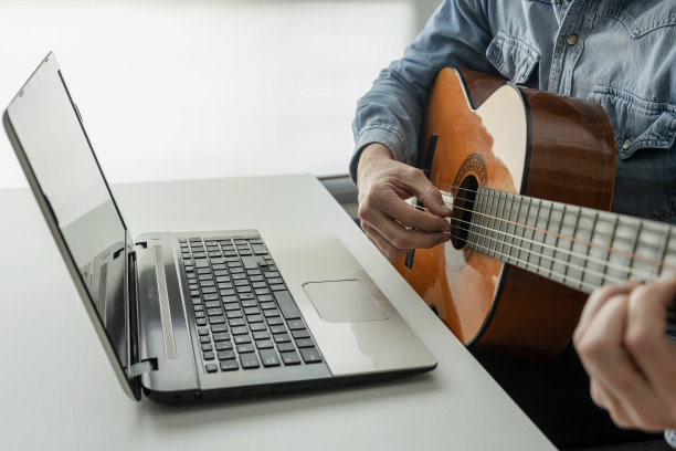 男人在家用笔记本电脑在线学习弹吉他。视频教程的概念。图片下载