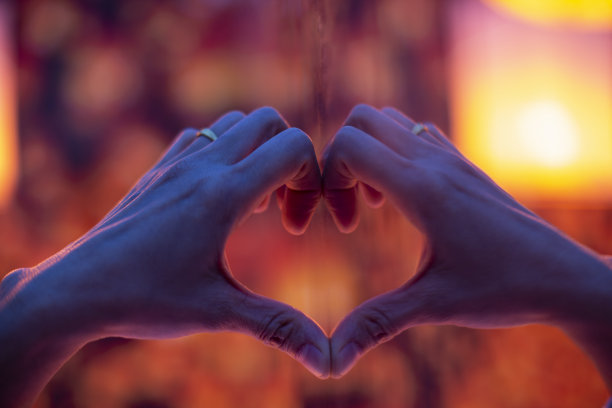 手在一个心形的形状与镜子与模糊的橙色背景。图片下载