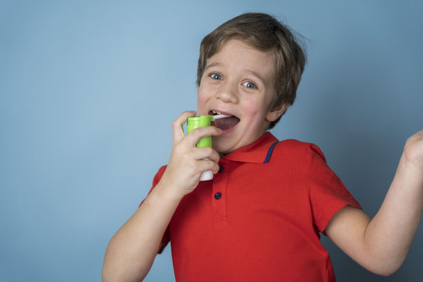 一个白人男孩把一种喷雾剂喷进嘴里治疗喉咙痛，这种喷雾剂是局部使用的。气溶胶吸入器图片下载