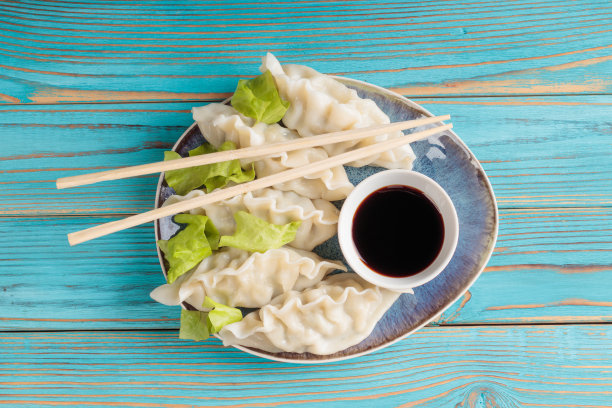 鲜煮的中国饺子与酱油蓝色木制背景。图片下载