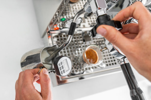 咖啡师在咖啡厅用蒸汽机煮咖啡和牛奶，用温度计在牛奶泡泡的时候检查温度图片下载