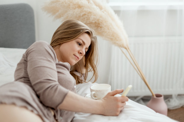 一个小女孩躺在家里的床上，用智能手机浏览社交网络图片下载