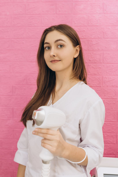 用于去除护士手中多余毛发的激光装置。激光脱毛，身体美容。美丽的理念。女孩在粉红色的背景下，手握脱毛器的工作部分图片下载