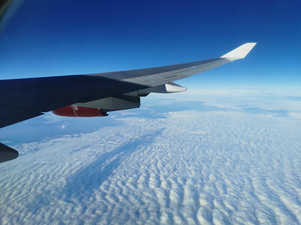 从一架飞机的机翼上的舷窗往外看，红色的飞机发动机在美丽的白云之上飞行。图片下载