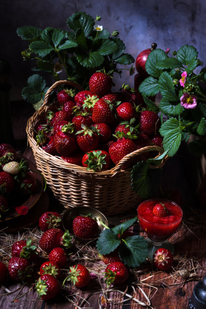 成熟的新鲜草莓在柳条筐在黑色的背景与绿色的叶子和粉红色的花在草莓植株上图片下载