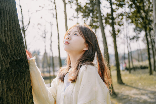 一个美丽的亚洲女孩在阳光下靠在一棵树上图片下载