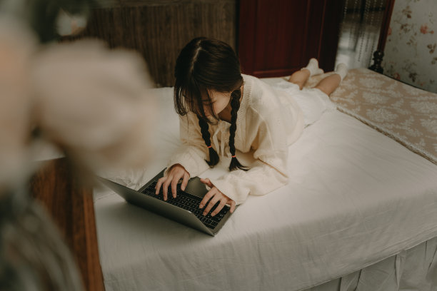 一个美丽的亚洲女孩在床上用电脑工作图片下载