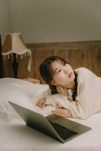 一个美丽的亚洲女孩在床上用电脑工作图片下载