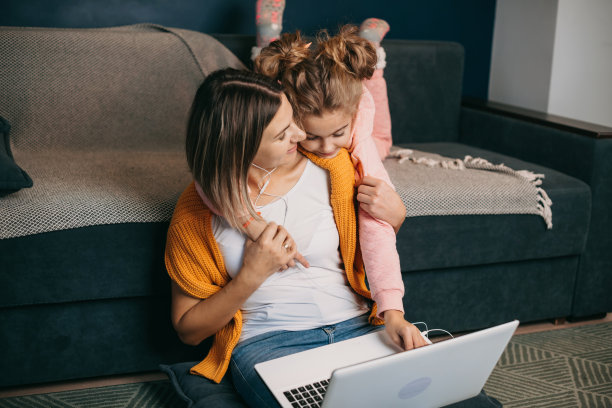 周日，女孩和妈妈坐在家里，听着高质量的音乐放松自己，拥抱和享受生活。幸福的家庭休闲。女人工作的笔记本电脑。通信技术。图片下载