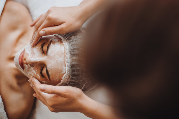 美容师在美容院用手将白色面膜敷在顾客脸上。前视图。美丽的皮肤。面部皮肤治疗。图片下载