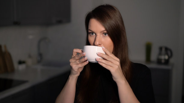 一位年轻女子端着一杯茶或咖啡享用早餐图片下载