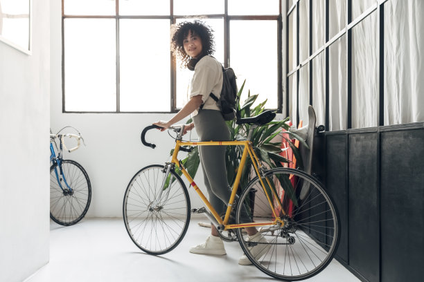 一个年轻的多种族妇女背着双肩包，骑着一辆黄色自行车从房子里走出来图片下载