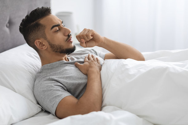 生病的阿拉伯青年男子躺在家里的床上咳嗽图片下载