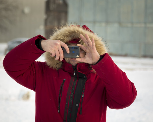 一名身穿红色羽绒服的男子正在用手机拍照图片下载