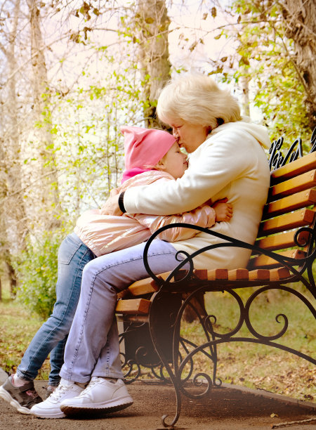 奶奶和她的孙女坐在公园的长椅上拥抱交谈。软的焦点。图片下载