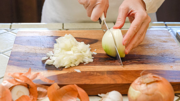 一个白人妇女用手在厨房台面的木板上切白洋葱图片下载