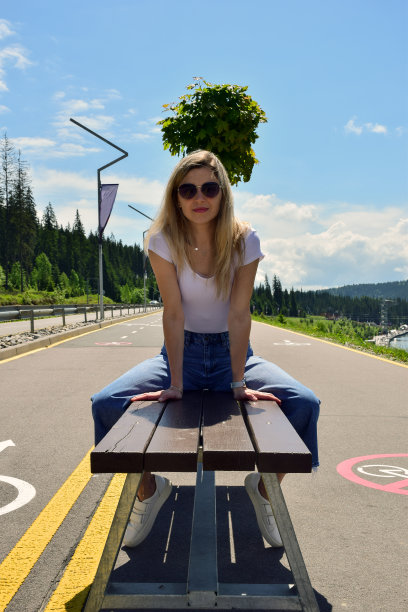 年轻漂亮的白人妇女坐在长椅上太阳镜，t恤和牛仔裤图片下载