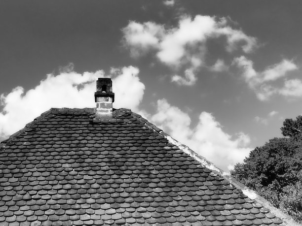 红色的屋顶上有一个烟囱，在蓝天白云下。传统的乡村瓦屋顶图片下载