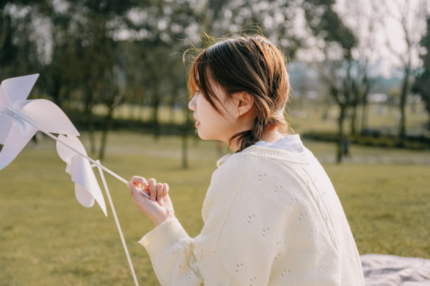 一个美丽的亚洲女孩和一个纸风车在黄昏的草坪上图片下载
