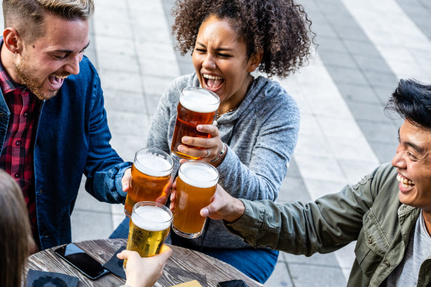 年轻人聚在一起喝啤酒，z世代的男人和女人在一起玩乐，焦点放在酒杯上图片下载