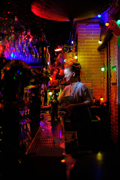 在酒吧或酒吧柜台后面工作的微笑的女酒保。图片下载