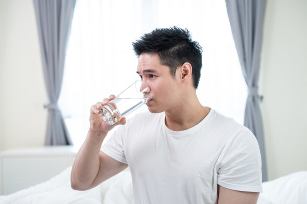 亚洲有吸引力的男性的肖像，在厨房里拿着一杯水。年轻饥渴的帅哥在清晨醒来后，为居家保健而斟上一杯纯净的天然矿物质图片下载