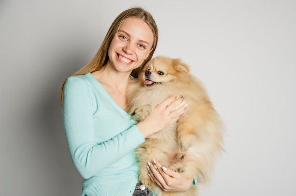 一个金发女孩抱着一只博美犬，看着镜头。肖像图片下载