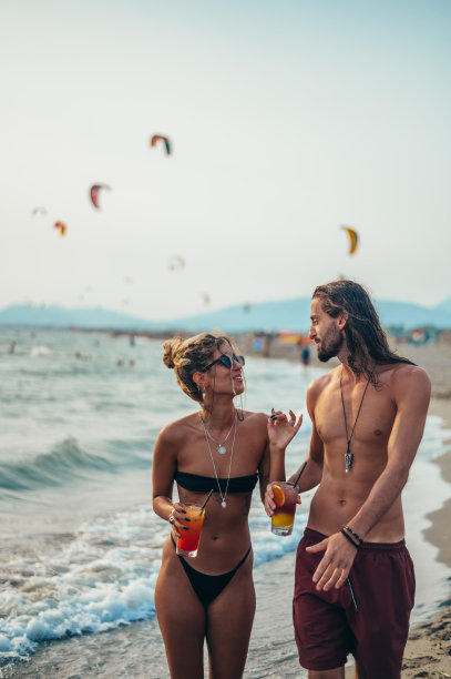 迷人的年轻夫妇带着酒精鸡尾酒在海滩上散步图片下载