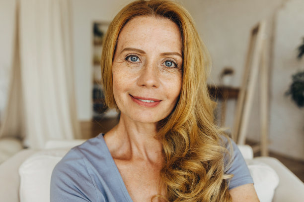 不化妆的50多岁白种人成年女性，有着天然的美丽，完美的衰老的皮肤，布满雀斑，一些面部皱纹和皱纹，坐在室内的背景下图片下载