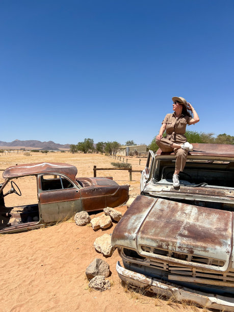 一名年轻女子穿着游猎服，坐在一辆废弃的旧生锈汽车的屋顶上图片下载