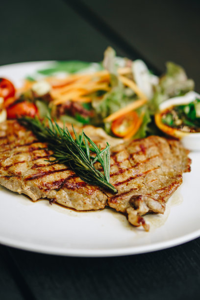 黑木桌上白盘子里的生菜肉排图片下载