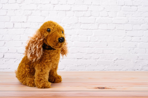 动物玩具:棕色的狗娃娃放在木制的桌子上，白色的砖墙图片下载