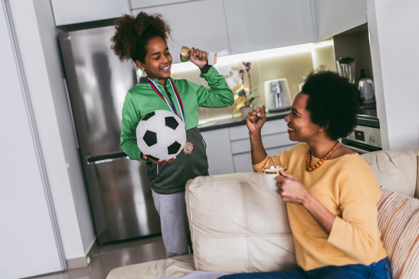 骄傲的母亲看到女儿在足球比赛后手里拿着奖牌和奖杯感到非常兴奋。图片下载