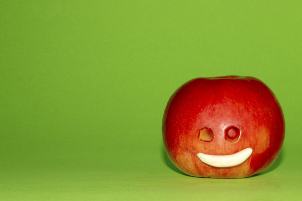 一个微笑的苹果在底部角落的绿色背景图片下载