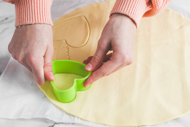 一个白人少女的手用绿色塑料心形切割器在白色羊皮纸上切下酥皮图片下载