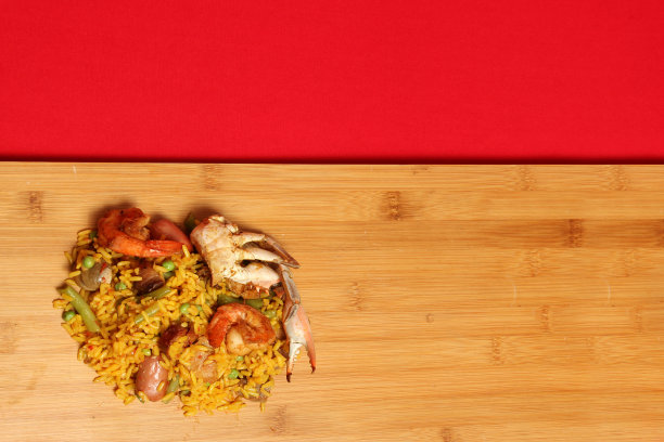 来自西班牙巴伦西亚的西班牙肉菜饭:红色背景的木板上的肉菜饭，搭配藏红花、海鲜、虾和蔬菜即可食用图片下载