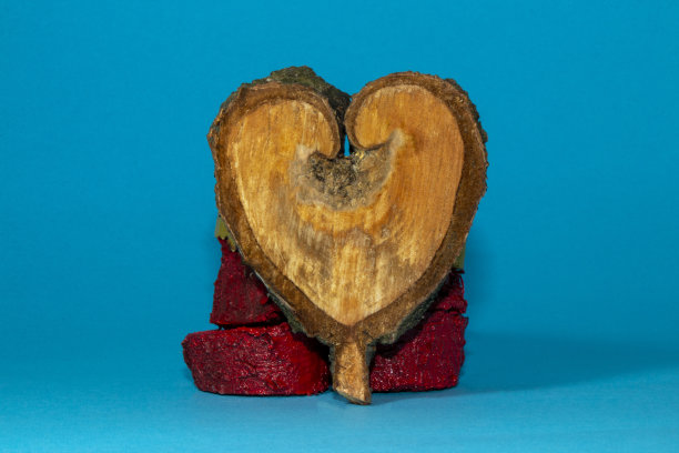 木材自然形状的心脏，倚靠在红色的树桩上，背景是柔和的蓝色图片下载