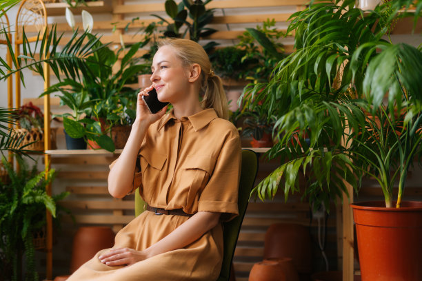 有吸引力的快乐的年轻女子花店老板坐在自己的花店和谈智能手机与客户。图片下载