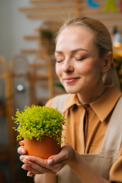 近距离的垂直镜头，漂亮的女花商在花店里，在围裙上闻着紫菜盆花，闭着眼睛。图片下载